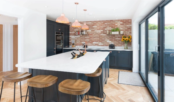Contemporary kitchen with wooden floor, dark cupboards and white top and brick wall